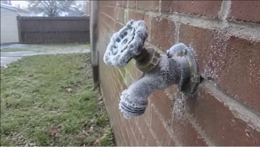 Outdoor spigot covered in thick frost mounted on a brick wall, illustrating freezing risk for a winter plumbing checklist in Nebraska